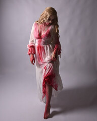  Full length portrait of  scary vampire zombie bride, wearing elegant halloween fantasy costume  dress with bloody red paint splatter. in standing walking pose. Isolated on studio background 
