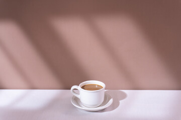 A cup of coffee with a brown wall background with window shadows
