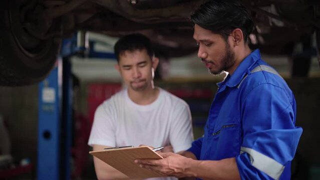 Asian automotive Mechanic man and a customer explain car condition discussing repairs problems to his vehicle in mechanics workshop point and auto service garage.