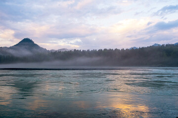A wide, full-flowing mountain river with a fast current at dawn or sunset. Mountains and forest in the fog. A large turquoise-colored mountain river Katun in the Altai Mountains, Altai Republic.