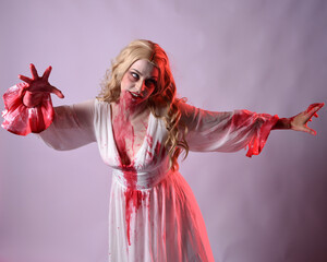 Close up portrait of  scary vampire bride wearing elegant halloween fantasy costume bloody splatter. Isolated on studio background with gestural hands reaching out towards camera.