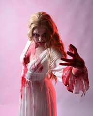 Close up portrait of  scary vampire bride wearing elegant halloween fantasy costume bloody splatter. Isolated on studio background with gestural hands reaching out towards camera. © faestock