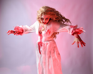 Close up portrait of  scary vampire bride wearing elegant halloween fantasy costume bloody splatter. Isolated on studio background with gestural hands reaching out towards camera.