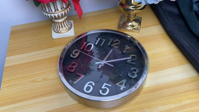 Hand using dust whisk to sweep dirt from dead wall clock on the wooden table in office room.