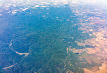 Aerial view from airplane window above green ground. View from the airplane window with beautiful clouds at sunrise