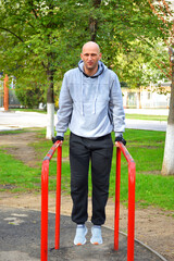 a young bald man doing push-ups on parallel bars in a city park. active lifestyle, physical...