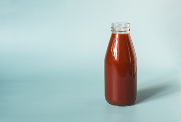 Glass bottle with tomato juice close-up on a light background