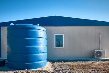 Blue plastic water tank stands next to prefabricated industrial building. Newly built single storey...