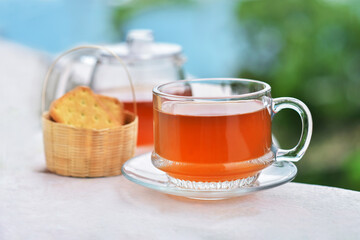 Cup of herbal infusion tea with biscuits basket and teapot background. This hot drink for afternoon tea, hight tea, elevenses, and cream tea