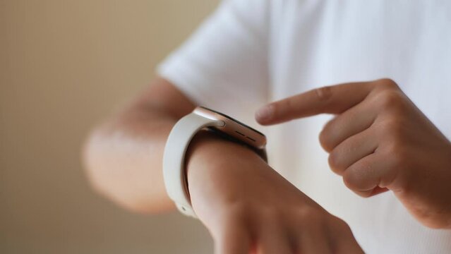 Close-up cropped shot of unrecognizable little preteen girl using modern smart watch touching button and touchscreen while posing indoors on isolated background, touching button, setting smart watch.