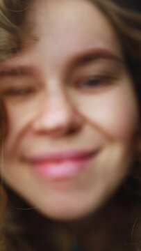 close-up of the face of a curly-haired girl who takes off her glasses and smiles at the camera. the girl bites her lip and dances. macro eye the woman is fooling around. vertical video