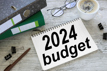 Budget 2024 open notepad with text. two folders for documents. a cup of coffee