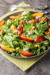 Fresh salad of plums, arugula, gorgonzola cheese and walnuts close-up in a plate on the table. Vertical