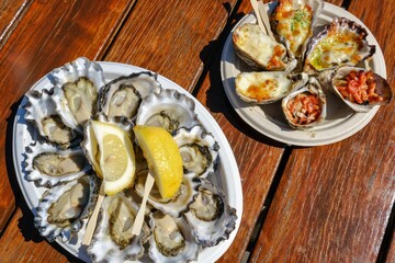 A plate of fresh Sydney rock oysters with lemon wedges and a smaller plate of grilled oysters with assorted toppings (garlic cheese, mornay, bacon) at Jim Wilds Oyster Shack, Greenwell Point, NSW