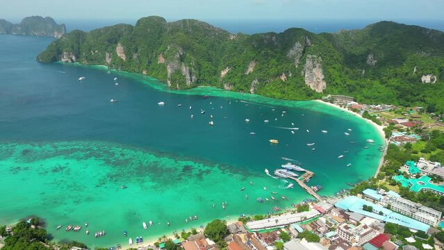 A phenomenal aerial shot of Pi Ley Bay: countless boats are moored near the shore, where a rural village is located below the mountains, Thailand