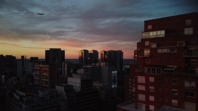The plane flies through the evening sky of Buenos Aires, landing over the city, sunset, blue sky, building, drone view