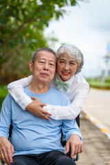 Fototapeta premium Nature harmony, Asian elderly couple happiness in the outdoor park, Elderly husband on wheelchair, wife caregiving, park outdoor, happy family, grey hair, hug, kiss