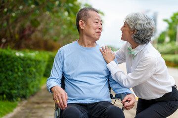 Fototapeta premium Nature harmony, Asian elderly couple happiness in the outdoor park, Elderly husband on wheelchair, wife caregiving, park outdoor, happy family, grey hair, hug, kiss