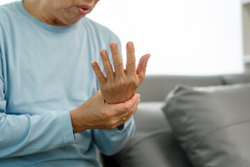 Elderly Asian gentleman with wrist discomfort on the couch, expressing pain due to Carpal Tunnel...