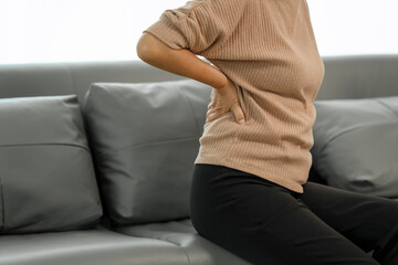 Elderly asian woman sitting on the couch, back pain, osteoporosis.