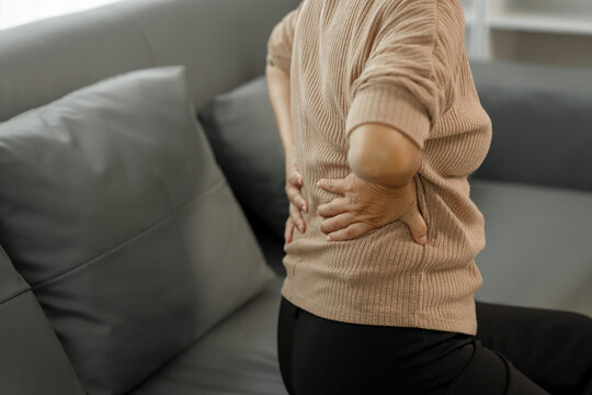 Elderly asian woman sitting on the couch, back pain, osteoporosis.