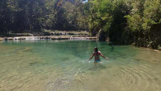 Latin female in blue bikini walks into green tropical forest river