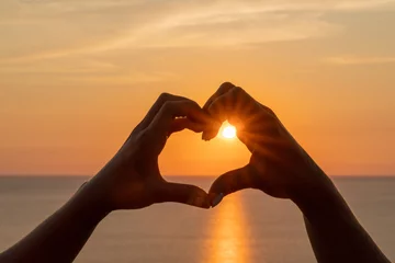 Fototapeten Hands heart sea sanset. Hands forming a heart shape made against the sun sky of a sunrise or sunset on a beach © svetograph
