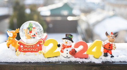 Looking forward to the Christmas holidays. Happy New Year 2024 - numbers in the snow, souvenir figurines of a snowman, deer, Santa. greeting card. winter holiday mood.