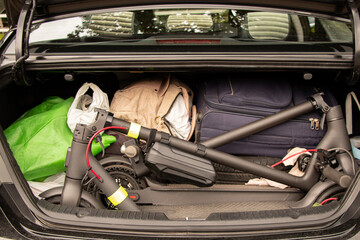 Two electric scooters and suitcases with things are in the trunk of a car that goes on vacation in...