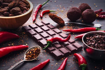  Dark chocolate bar, red hot chilli pepper cayenne,  dry hot chili spices, cocoa beans nibs powder, food tasty design on black wooden background © ValentinValkov