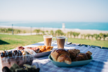 A picnic at the seaside beach. Breakfast with coffee, croissants and donuts by the ocean shore