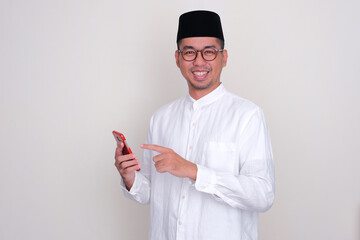 Moslem Asian man smiling happy and pointing to mobile phone that he hold