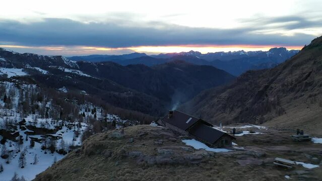 Drone over Bivacco Marino Bassi mountain cabin with epic sunset view down valley