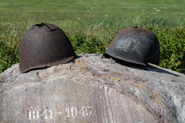 Old rusty military helmet with holes lie at the memorial world war years 1941 1945 on stone - obrazy, fototapety, plakaty