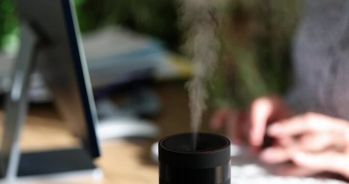Woman hand is typing on computer keyboard and diffuser diffuses fresh scent. Female worker enjoying aroma of essential oils in office