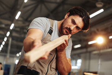 Young carpenter man looking and choosing wood plank at workshop in carpenter wood factory