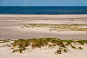 Fototapeta na wymiar Strandköbe auf einem leeren Sandstrand im Vordergrund eine Düne mit bilck über die Nordsee bis zum Horizont