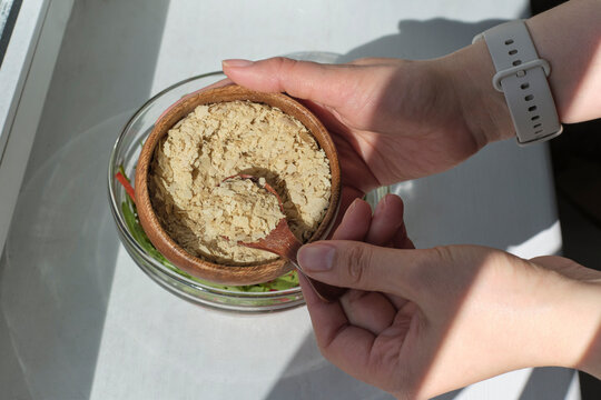 Flavor Meets Nutrition: In a kitchen lit by the soft glow of evening, a woman's hand artfully adds a sprinkle of nutritional yeast to a salad, merging the worlds of taste and wellness in one simple