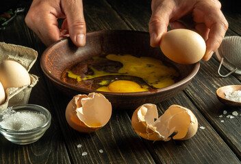 Cooking eggs for breakfast at home. Healthy egg diet concept. The cook is trying to break an egg on a plate on the kitchen table
