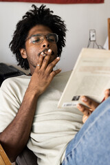 Afro boy relaxing on the sofa at home while reading a book. Vintage vertical photo