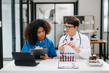 Focused mature male doctor and African female nurse look at tablet and laptop discuss anamnesis together. Concentrated diverse medical professionals in hospital.