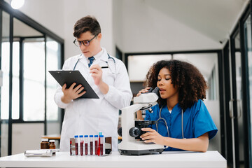 Focused mature male doctor and African female nurse look at tablet and laptop discuss anamnesis together. Concentrated diverse medical professionals in hospital.