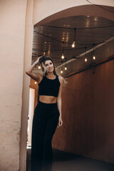 Beautiful blonde model woman, fashionable in a black suit, poses against the walls of a building