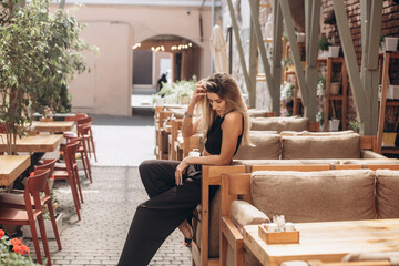Beautiful blonde model woman, fashionable in a black suit, posing in a cafe