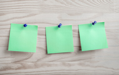 Three green paper notes pinned to wooden bulletin board. Mockup green paper note pad attached with push pin on wood background