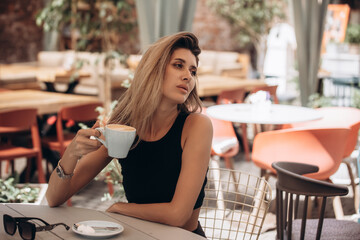 Beautiful blonde model woman, fashionable in a black suit, posing in a cafe