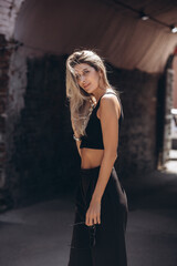 Naklejka premium Beautiful blonde model woman, fashionable in a black suit, poses against the walls of a building