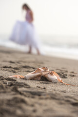 Pointe shoes on the sand , a ballerina in the background.