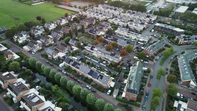 Aerial view of a beautiful suburban neighborhood with solar panels on rooftops. The cameras tilts up and reveals a gorgeous and golden sunset