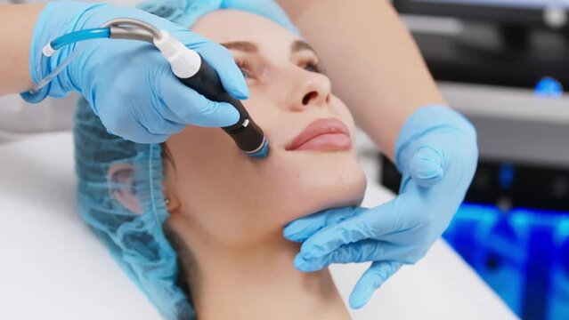 Professional dermatologist in medical gloves doing hydro peeling procedure for beautiful woman patient in cosmetology clinic. Close up facial treatment.